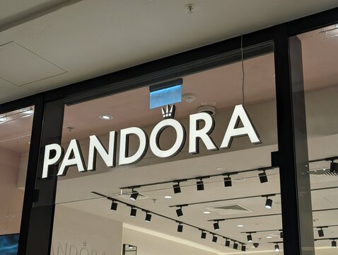 Warsaw, Poland,May 03, 2026. Modern glass facade storefront displaying the glowing corporate white Pandora jewelry boutique brand logo sign. High quality photograph.