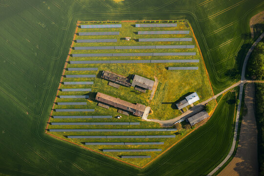 Aerial view of a solar farm with rows of photovoltaic panels surrounding old farm buildings in a rural landscape in Chvalkovice, Hradec Kralove Region, Czechia.
