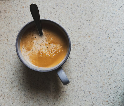 Overhead view of a coffee cup with fresh coffee in calm tones with speckled benchtop with copy space