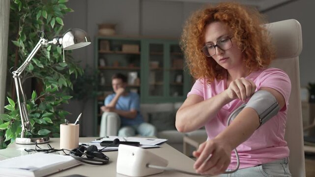Woman measuring blood pressure with tonometer at home