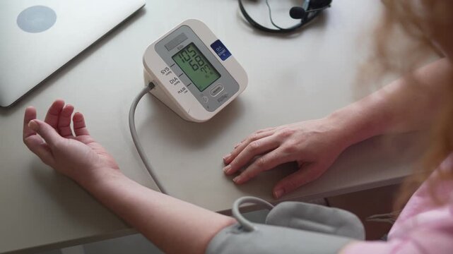 Woman measuring blood pressure with digital tonometer at home