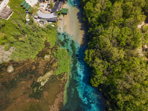 Aerial view of the Blue Eye natural spring with its vibrant turquoise water surrounded by lush green forest and small structures in Finiq, Vlore County, Albania.