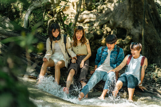 Young Asian man and woman friends relaxing together by waterfall lagoon at tropical forest enjoying eco tourism adventure outdoor travel active lifestyle nature therapy on summer holiday vacation.