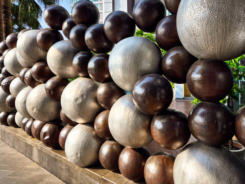Modern outdoor abstract sphere sculpture with metallic textures in an urban plaza, featuring geometric design, depth, and architectural background.