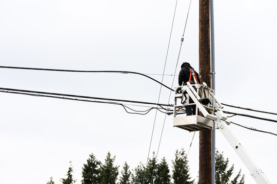 Power company lineman working on electrical lines from a lift bucket, upgrading service to residential neighborhood, workman wearing hard hat and safety harness

