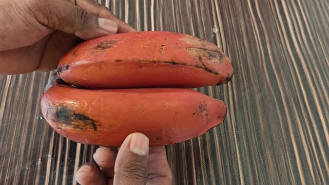 Hand placing red banana bunch on a wooden surface