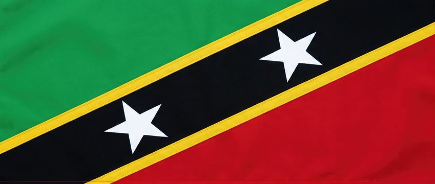 Close-up shot of the flag of Saint Kitts and Nevis with its bold diagonal black band bordered by yellow, a red triangle on the bottom and a green triangle on the top.