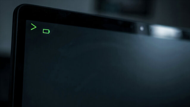 Close up of a laptop screen displaying a command line prompt and a battery icon in a dark room