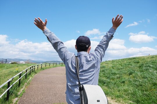 青空と草原を前に万歳する男性の後ろ姿