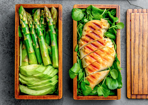Take away concept. Grilled chicken and avocado with asparagus and green salad in wooden japanese bento box. Top view, slate gray background