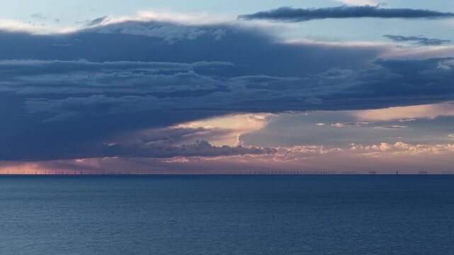 Aerial wide view of offshore sea wind farm with storm clouds at sunset