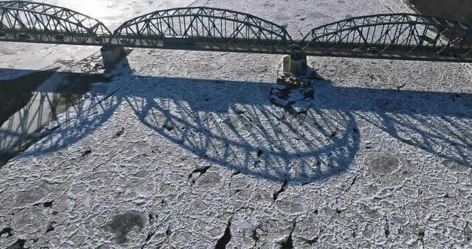 Old metal bridge with traffic over river with ice floes.