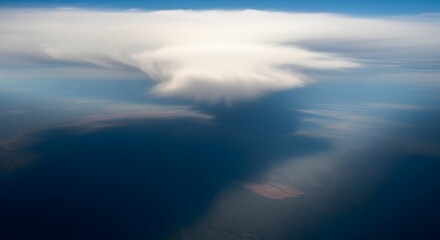 Obraz premium High altitude aerial view showing a massive white storm cloud casting a dark dramatic shadow across vast landscape under bright blue sky