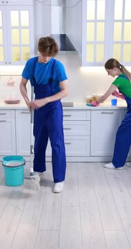 Teenage workers cleaning kitchen and mopping floor indoors. Part-time job