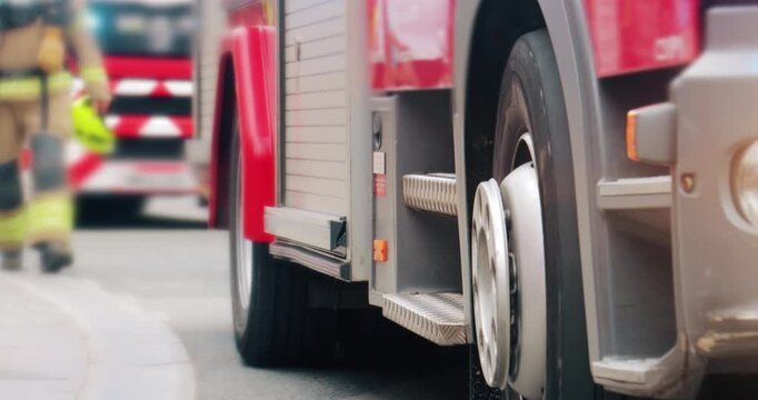 Firefighter by fire truck emergency services vehicle. Fireman in department uniform and two red fire engine appliances with flashing lights used by brigade during accident response and rescue duty.