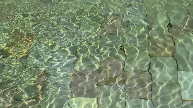 Sunlight reflecting beautiful water caustics on the tiled floor of a shallow pool.