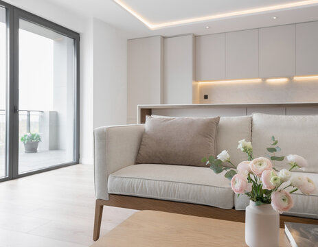 A close-up of a very modern living room featuring simple, concealed modern lighting and floral accents; the new furniture avoids a futuristic look, complementing the open-plan layout shared with the k