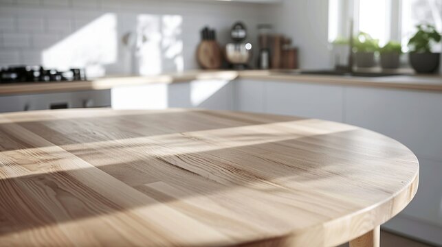Close-up view of a light wooden round kitchen table with a bright, modern kitchen blurred in the background