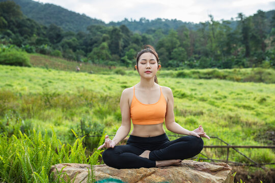 A serene young woman practices meditation outdoors on a large rock embodying peace wellness and connection with nature.