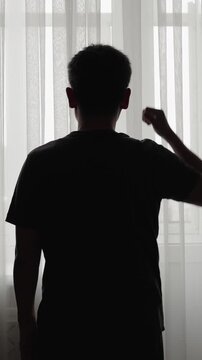 Back view of stressed adult man standing alone by the window and holding his head. Concept of anxiety, burnout, life problems, loneliness, depression and emotional crisis. Vertical video.