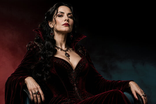 Elegant mature dark queen wearing luxurious deep red velvet gown, mysterious gothic royalty portrait, powerful fantasy woman, dramatic cinematic fashion isolated on dark background