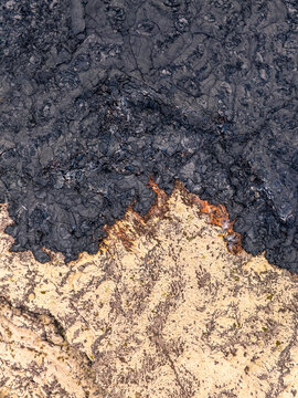 Aerial view of solidified black lava flow contrasting with light volcanic terrain in Iceland.