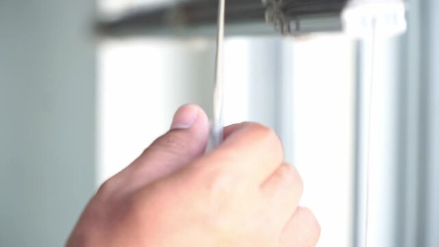 hand adjusting window blinds with a pull cord. Natural illumination, privacy adjustment, and modern residential living concept.