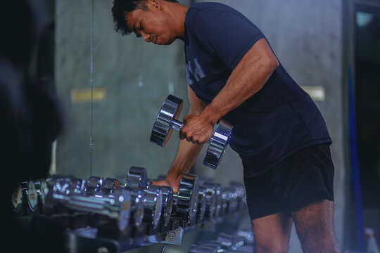 Young man with sweat doing exercises, working out with dumbbell in fitness gym. Strong and healthy concept. Selected focus