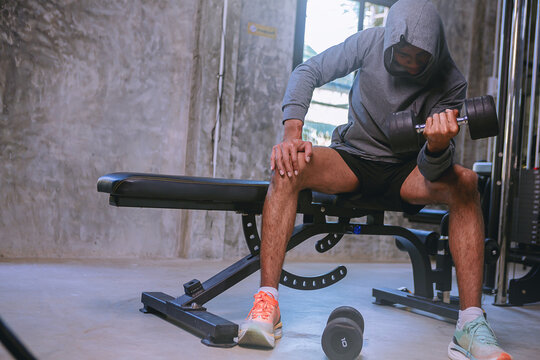Young man with sweat doing exercises, working out with dumbbell in fitness gym. Strong and healthy concept. Selected focus
