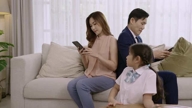 Asian family devices addicted to overusing social media to the point that they ignore their daughter and do not pay attention to each other dad and mom play phone while girl play game in living room. 