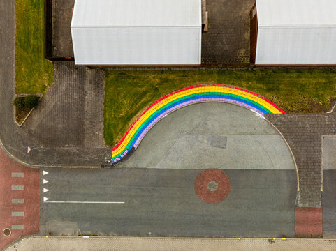 Aerial view of a vibrant rainbow-painted curb bordering a paved area next to a building with white roofs and road markings in Iceland.
