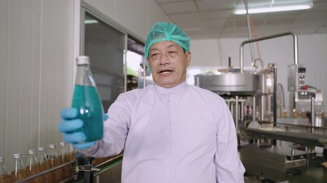 Professional Asian inspector in uniform of food and drink factory holding a juice beverage bottle promoting and advertising healthy nutritional benefits in production line at a manufacturing industry.