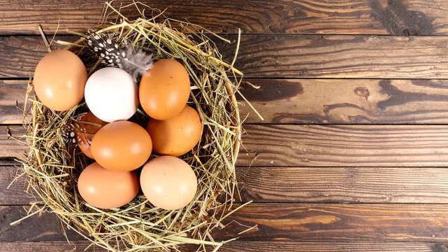 Brown and white eggs arranged in a straw nest on rustic wood.