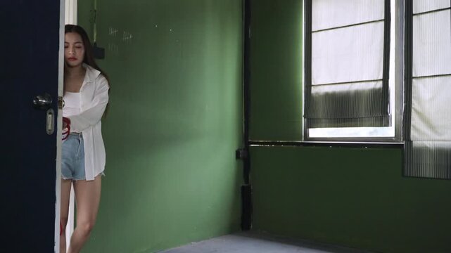 Unhappy and depressed Asian woman with mental health issues holding a red rope and dragging a chair in her room at home. A lonely female is stressed and worried about a failed life. Suicide concept. 