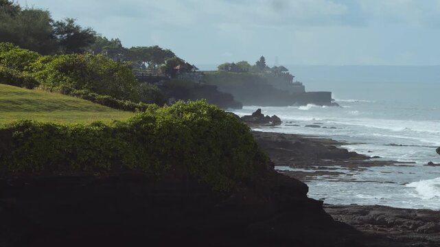 Coastal Tanah Lot Temple Silhouette At Sunrise, Misty Cliffs And Gentle Surf, Distant Pagoda On Rocky Promontory, Serene Pilgrimage Mood, Drone Travel Sweep, Soft Teal Tones And Slow Reveal,Bali.