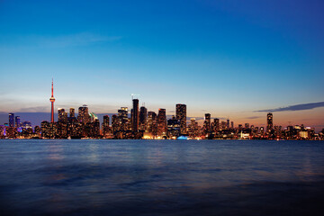Obraz premium Toronto skyline at dusk with illuminated city lights reflecting on the water, vibrant urban night view. g.