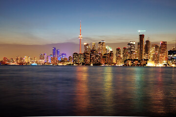 Obraz premium Toronto skyline at dusk with illuminated city lights reflecting on the water, vibrant urban night view. g.