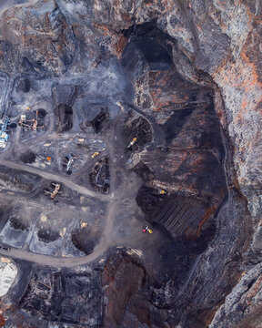 Aerial view of an open-pit mine with heavy machinery, excavated dark soil, and winding access roads in Iceland.