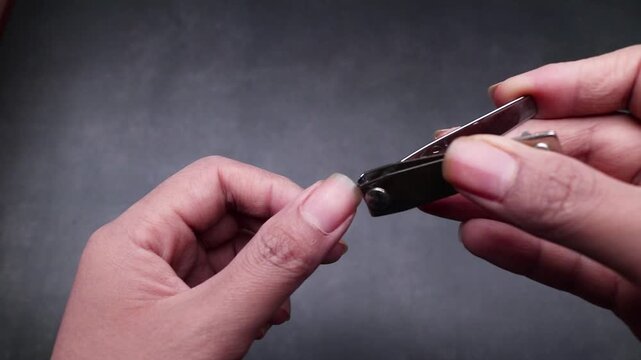 Close up detail of a hand cutting nails showing long, uncut, dry, and dirty fingernails, isolated on gray background.