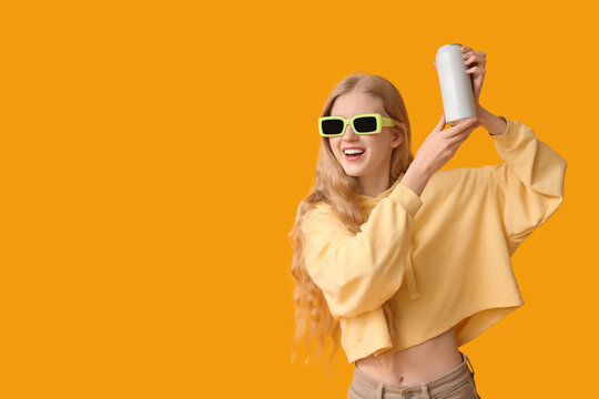 Beautiful young woman in sunglasses with can of soda on yellow background