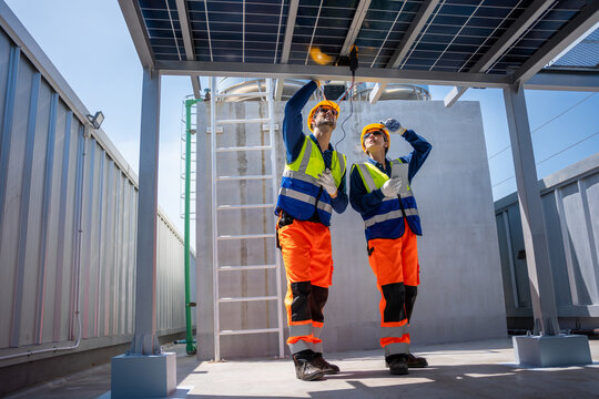 Engineers with digital tablet and multimeter inspecting solar panels on rooftop, Solar power technicians testing photovoltaic system equipment on building roof, Team of workers installing solar panels