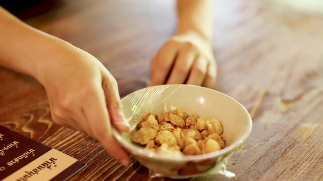 Hands Unwrapping Bowl of Crispy Pork Cracklings on Wooden Table
