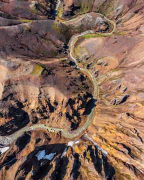 Aerial view of a winding river flowing through rugged volcanic terrain with patches of moss and snow in Iceland.