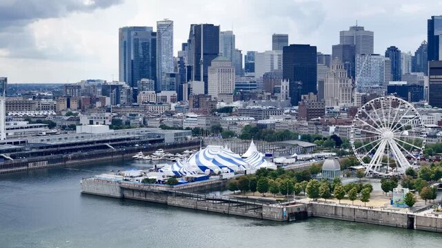 24th of June 2026 drone flight above the Cirque du Soleil blue-white tent at Montreal Old Port with city skyline in background. g.