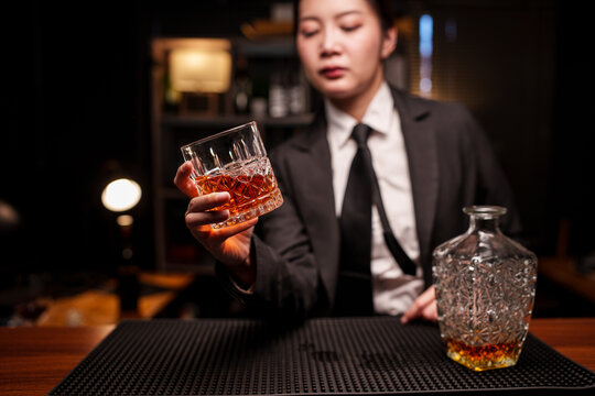 Woman bartender in a suit is handing a glass of whiskey across the bar counter.
