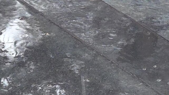 Soft rain falls on black tiled entrance steps. Gentle ripples dance on the glossy, damp surface as nature unfolds peaceful seasonal shower. Delicate watery reflections capture the calm, soothing mood.