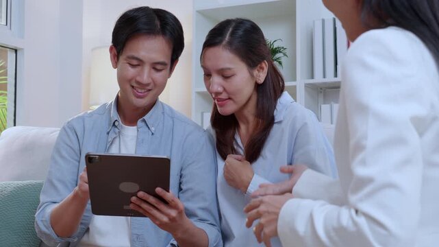 Asian couple signing digital contract on tablet screen during meeting, happy husband and wife signing electronic signature on tablet, clients approving digital insurance contract or investment.