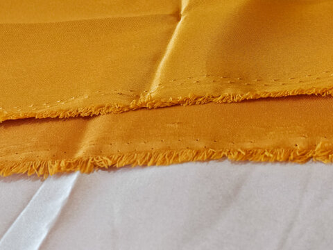 Macro close-up of orange satin fabric with visible textile weave and frayed edge detail, captured under soft natural lighting, ideal for luxury fashion backgrounds, design templates, and abstract text