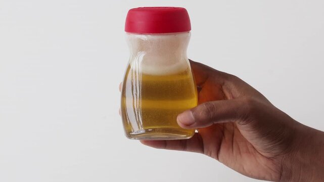 Close-up of a female hand presents a transparent jar containing raw bee honey with foam at the top. This package represents healthy breakfast ingredients and dietary supplements.