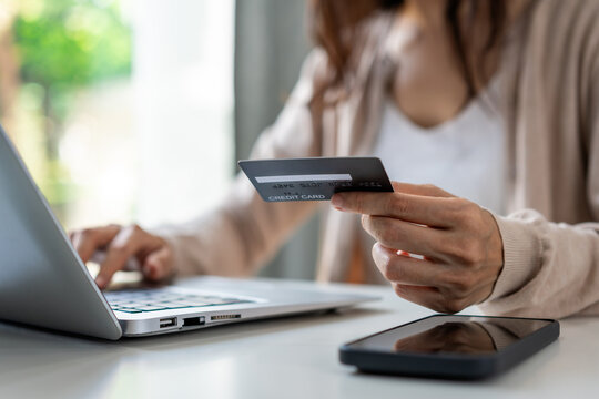 Young Asian woman using a credit card and smart phone for online shopping and mobile payment at home